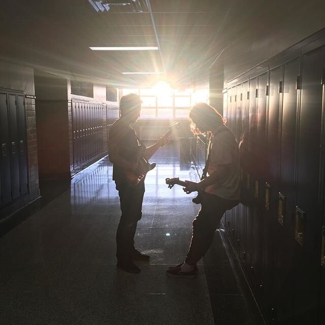 Two students playing guitars in a hallway