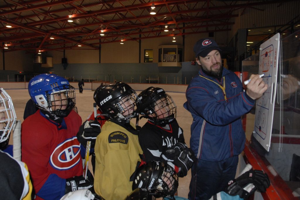 Joé Juneau coaching a group of players on the ice.
